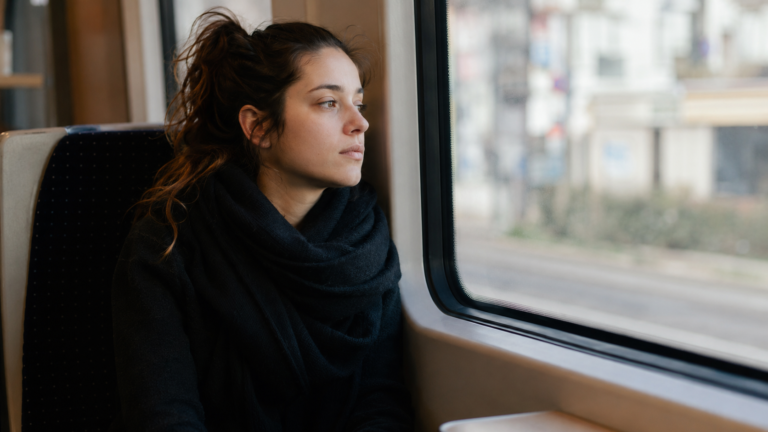 Mujer mirando por la ventana del transporte público con expresión distante, reflejando cómo la mente divaga del momento presente