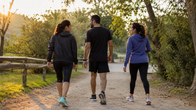 Tres adultos caminando por un sendero natural al atardecer, representando los beneficios de caminar para la salud mental y el bienestar emocional.